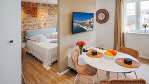 A bedroom with a stone wall, a bed, a TV, and a dining area with wicker chairs and a table. - Lucio Suites- Apartment 2 (Split)