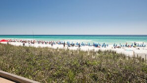 A beach with white sand, clear turquoise water, and a line of blue beach chairs and umbrellas.