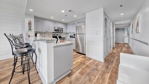 A modern kitchen with white cabinets, stainless steel appliances, and a wooden floor.