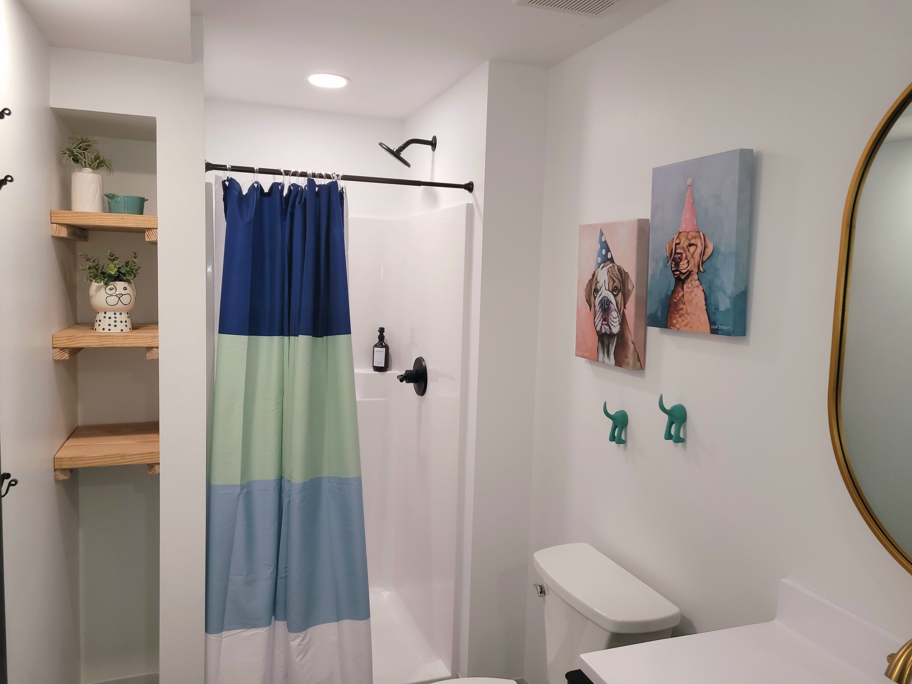Une salle de bain équipée d’un rideau de douche, de toilettes, d’un lavabo et d’éléments décoratifs, notamment une plante en pot et des tableaux encadrés.