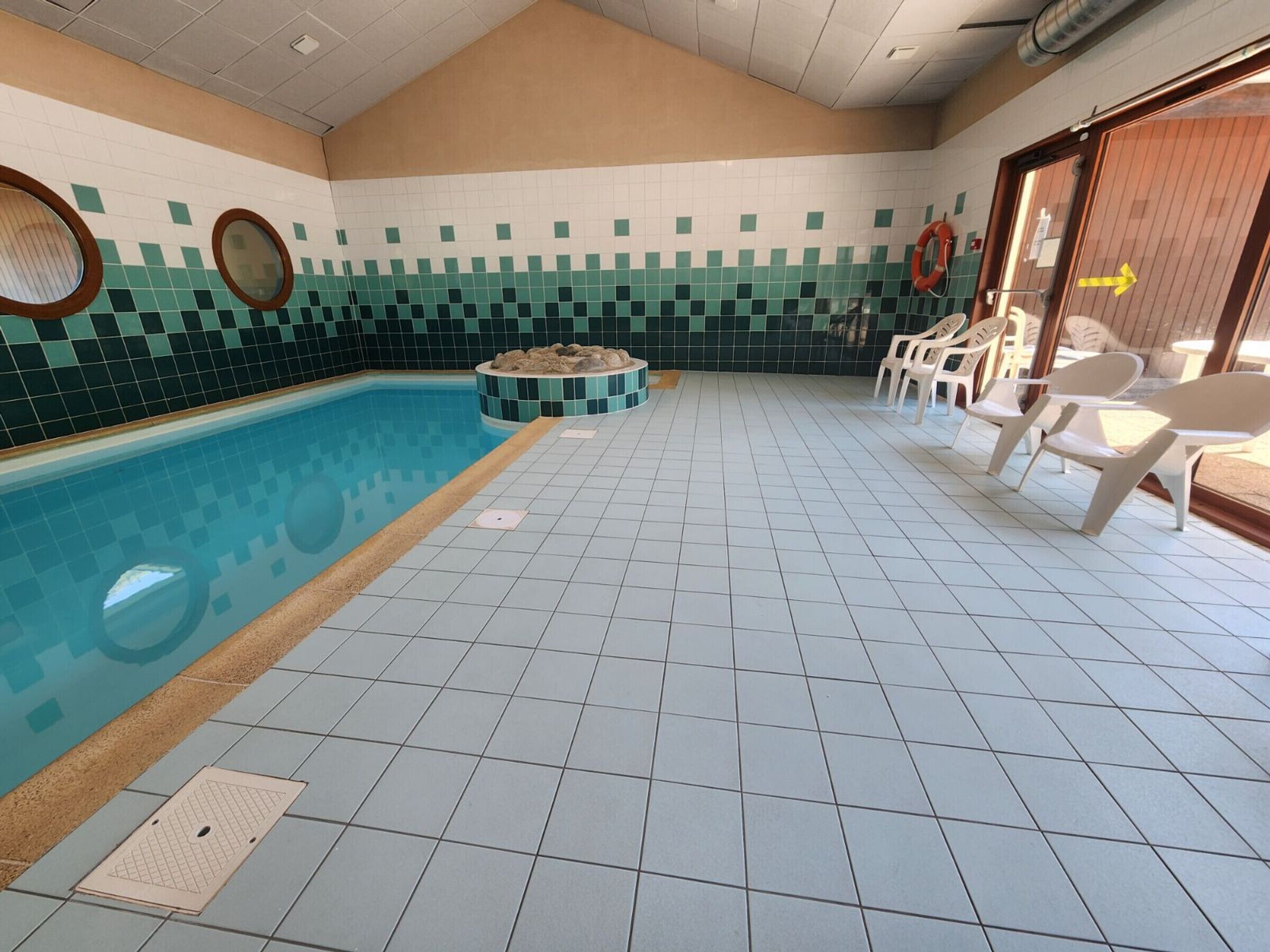 Une piscine aux murs et au sol recouverts de carreaux, entourée de chaises longues et d’une bouée de sauvetage.