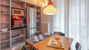 A dining area with a wooden table, chairs, a tray with food and drinks, and a kitchen area with appliances and shelves. - BnButler - Brivio 21 (Milan)