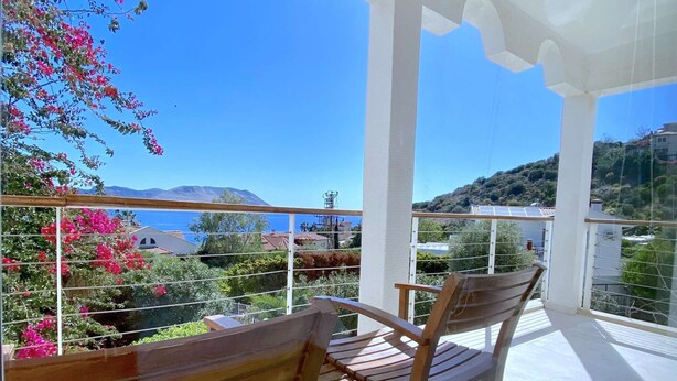 Un balcon avec des chaises en bois et une vue sur la mer et les collines.
