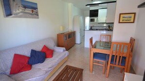 Uma sala de estar com sofá, almofadas vermelhas e azuis, mesa de centro de madeira e mesa de jantar com tampo de vidro e cadeiras de madeira.