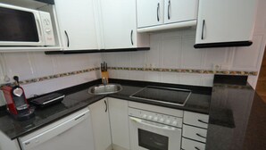 Uma cozinha compacta com armários brancos, bancada preta, micro-ondas, cafeteira, pia e fogão.
