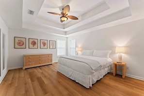 A bedroom with a bed, a dresser, a ceiling fan, and wall-mounted lamps.