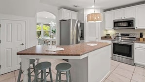 Een moderne keuken met witte kasten, roestvrijstalen apparatuur, een granieten aanrecht en een zitgedeelte met barstoelen.