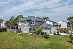 A two-story house with a grey exterior, a fenced backyard, and a small garden with palm trees.