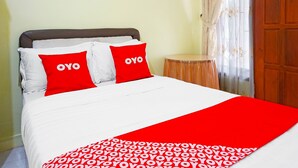 A bed with white and red bedding, two pillows with "OYO" text, a red blanket, and a wooden door in the background.
