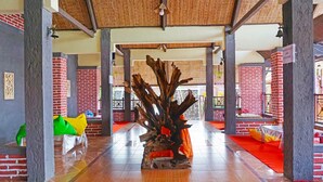 A spacious lobby with a central wooden sculpture, red brick walls, and a tiled floor.