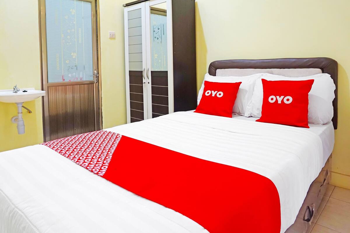 A bedroom with a bed, two red pillows with "OYO" text, a white bedspread, and a red and white patterned blanket.