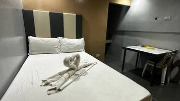 Hotelkamer met een bed, een netjes opgemaakt bed met een handdoek in de vorm van een zwaan, een klein tafeltje met een stoel, en een effen wand met een stopcontact.