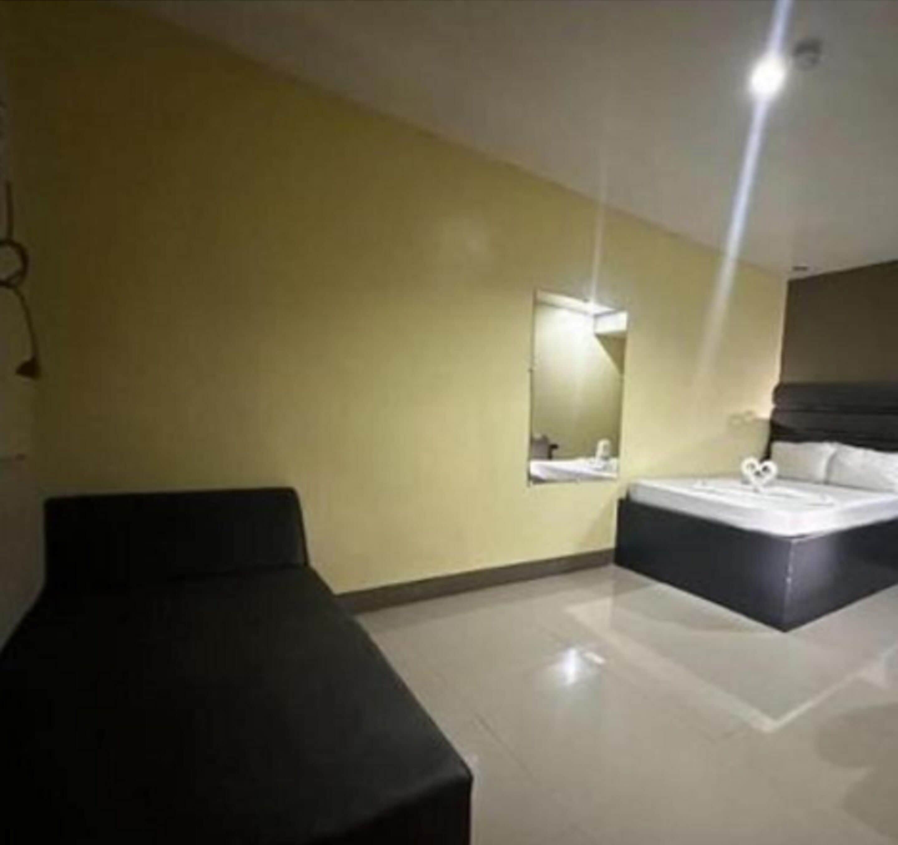 A hotel room with a bed, a bedside table, a mirror, and a black couch.