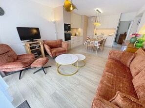 Un salon moderne comprenant un ensemble de canapés, un téléviseur, un coin repas et une cuisine en arrière-plan.