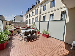 Une terrasse sur le toit, avec une table et des chaises, des plantes en pot et une vue sur le paysage urbain.
