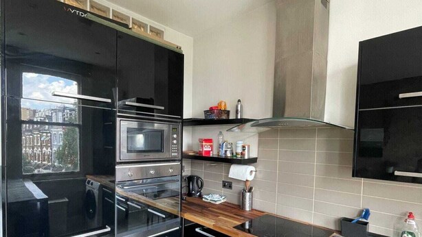 Una cocina moderna con armarios negros, horno de acero inoxidable, microondas y un ventanal con vistas a la ciudad.