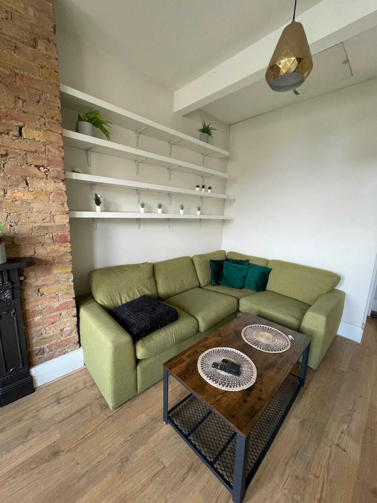 A modern living room with a green sectional sofa, a wooden coffee table, and white shelving with plants.