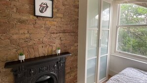 Un dormitorio con pared de ladrillo, chimenea, cama y ventana con vista a árboles.