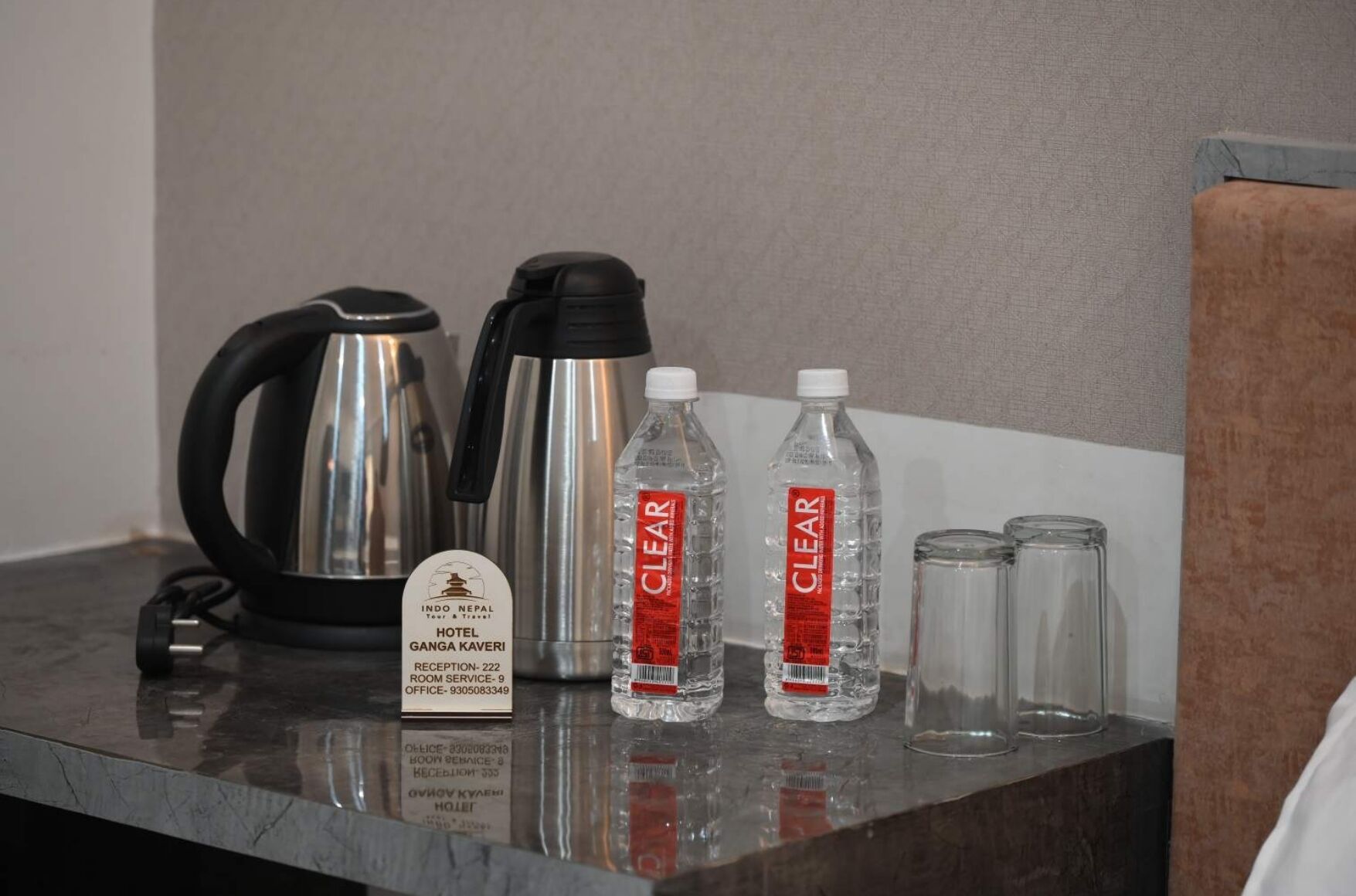 A hotel reception area with a kettle, two water bottles labeled 'CLEAR', and a sign indicating the hotel name and reception details.