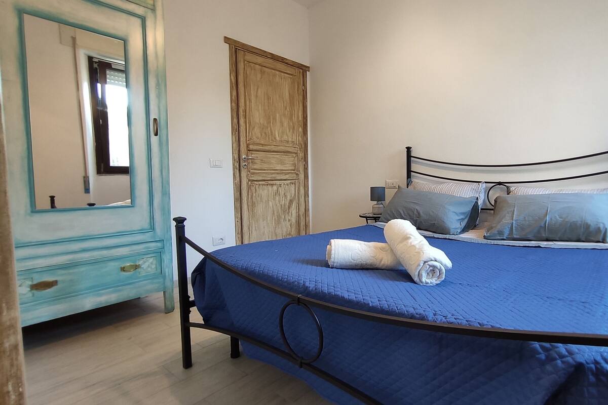 Une chambre à coucher comprenant un lit, une commode, un miroir, une porte et une table de chevet avec une lampe.
