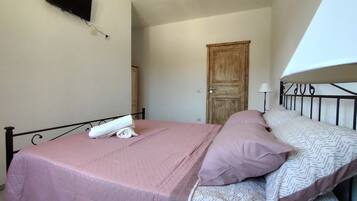 A single bed with a pink bedspread and pillows, a flat-screen TV mounted on the wall, and a wooden door in the background.