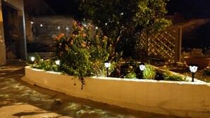 Un jardin illuminé la nuit, avec un parterre agrémenté de plantes fleuries, des luminaires décoratifs et un bac à fleurs blanc.