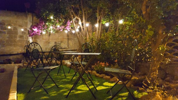 Un espace de restauration en plein air, avec une table et des chaises, entouré de verdure et d’un mur en pierre.