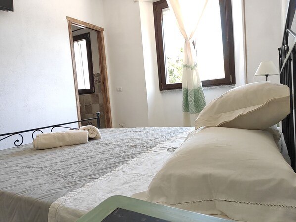 Un dormitorio con cama, ventana con cortinas, una puerta y televisor de pared.