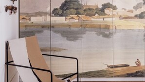 Une pièce avec un grand tableau représentant un paysage, une chaise et un tapis blanc.