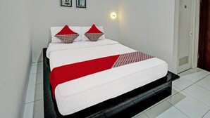 A neatly made bed with a white and red bedspread and matching pillows, a bedside table, and a wall-mounted light. - Hotel O Sirih Gading Family Guest House (Tulungagung)