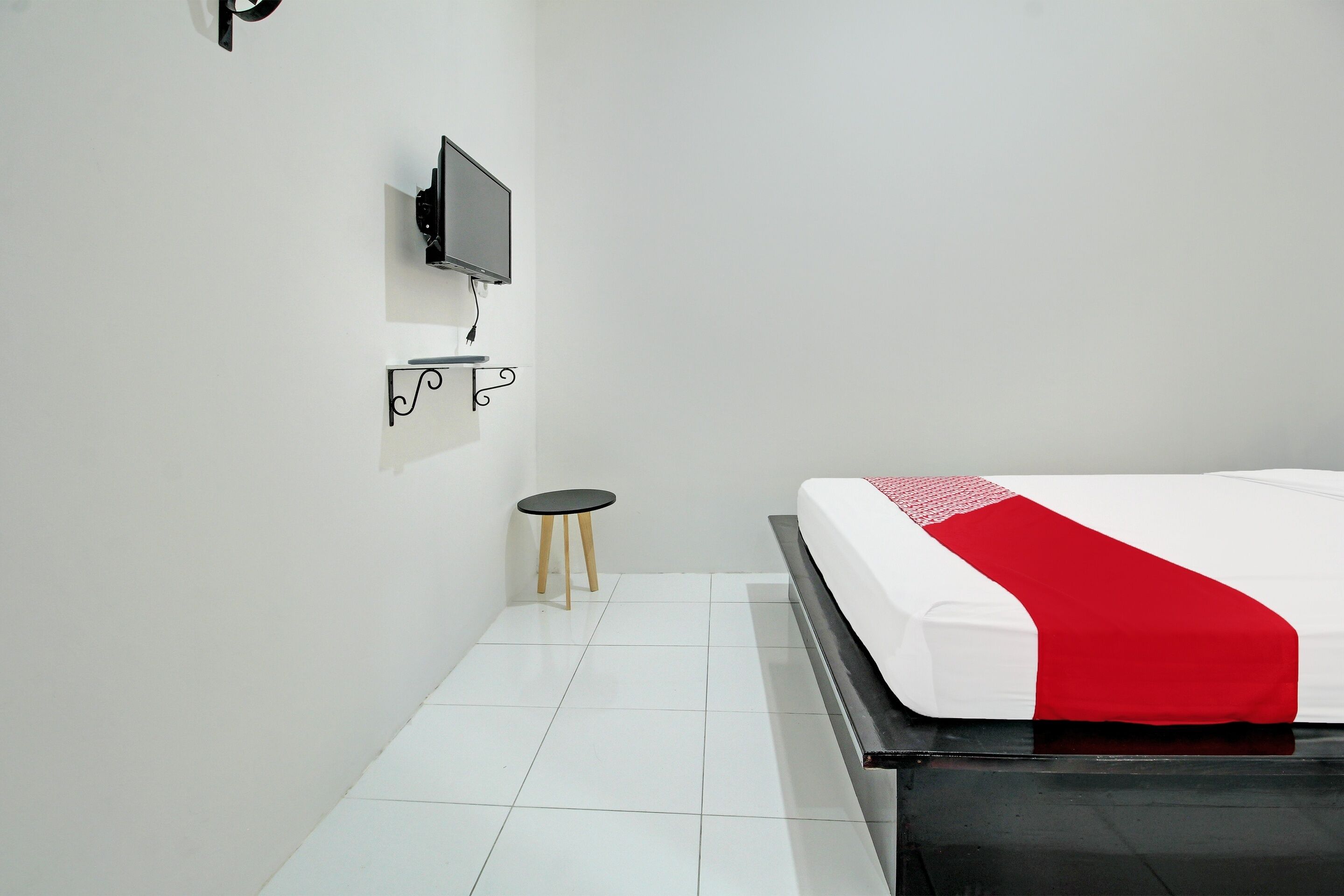 Une chambre d’hôtel avec un lit, un téléviseur fixé au mur et un petit tabouret.