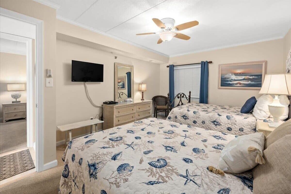 A bedroom with two beds, a ceiling fan, a TV, a desk, and a chair.