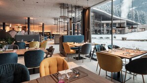 A modern restaurant with a view of a snowy mountain landscape. - Falkensteiner Family Resort Lido  (Chienes)