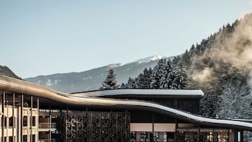 Ein modernes Gebäude mit gewölbter Dachkonstruktion, umgeben von schneebedeckten Bäumen und Bergen im Hintergrund.