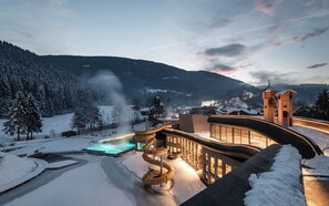 A snow-covered landscape with a modern building featuring a pool, a ski lift, and a church in the background.