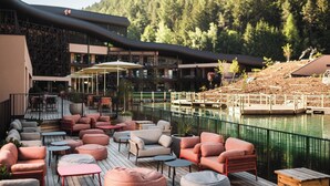 A deck with outdoor seating, a pool, and a view of a forested hillside. - Falkensteiner Family Resort Lido  (Chienes)