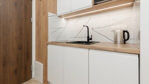 A modern kitchen with white cabinets, a black sink, and a microwave. - Air-conditioned Studio with Balcony | Close to EXPO XXI (Warszawa)