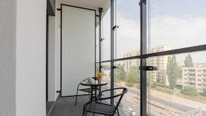 A balcony with a table and chairs, a door, and a view of a cityscape with buildings and a road. - Air-conditioned Studio with Balcony | Close to EXPO XXI (Warszawa)