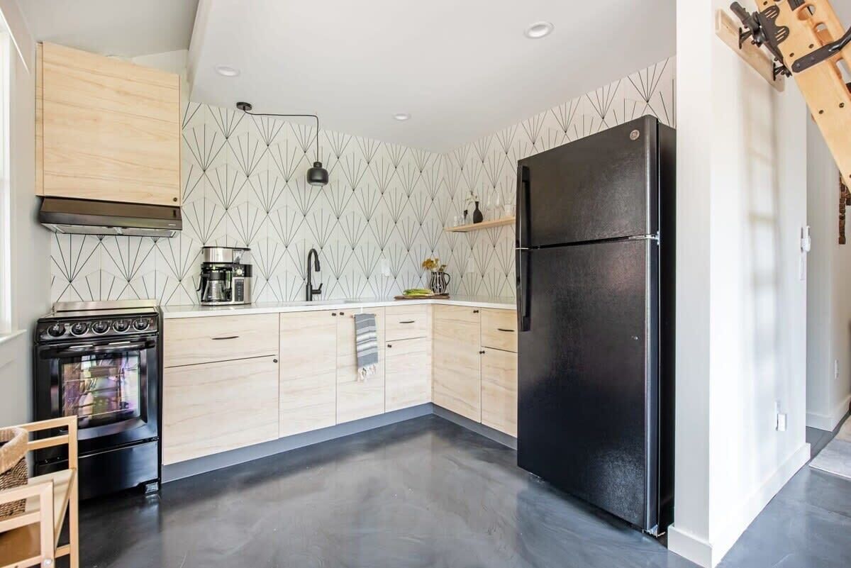 Een moderne keuken met een zwarte koelkast, houten keukenkastjes en een betegelde achterwand.