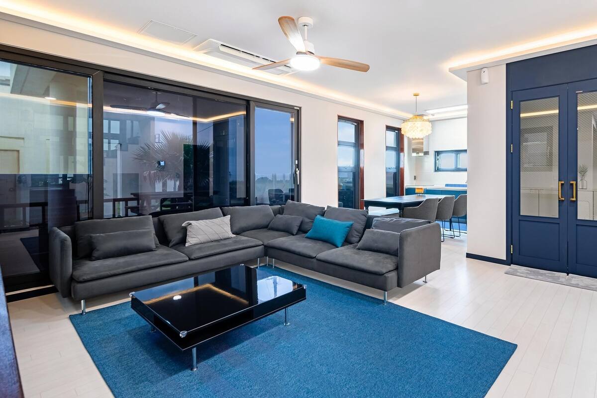 Ein modernes Wohnzimmer mit einer Eckcouch, einem Couchtisch und Blick auf die Stadt durch große Fenster.