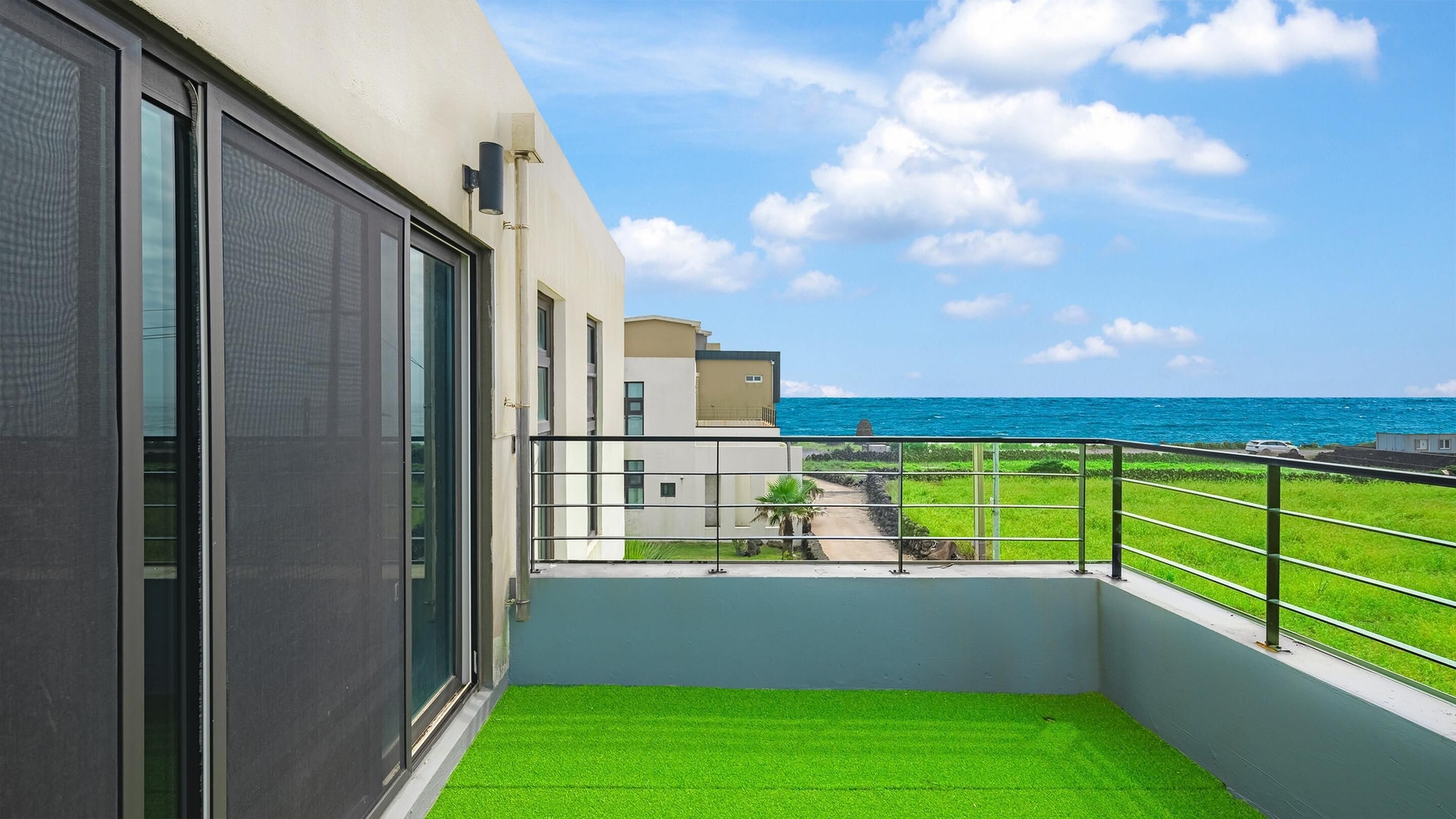 Un balcon avec un revêtement de sol synthétique imitant de l’herbe, une vue sur l’océan et un immeuble doté de grandes fenêtres.