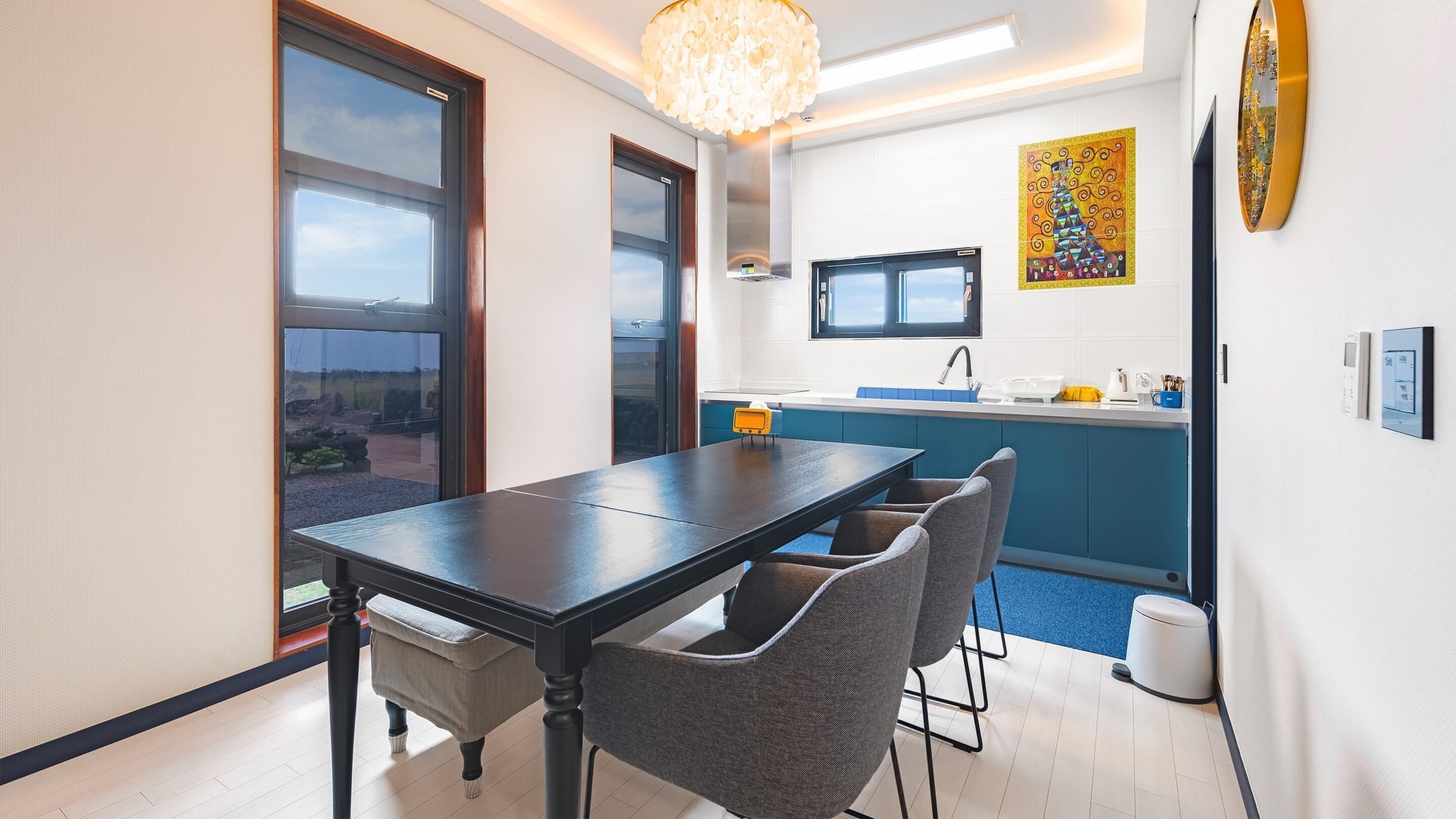 Eine moderne Küche mit großem Fenster, einem Esstisch mit Stühlen und Blick ins Freie.