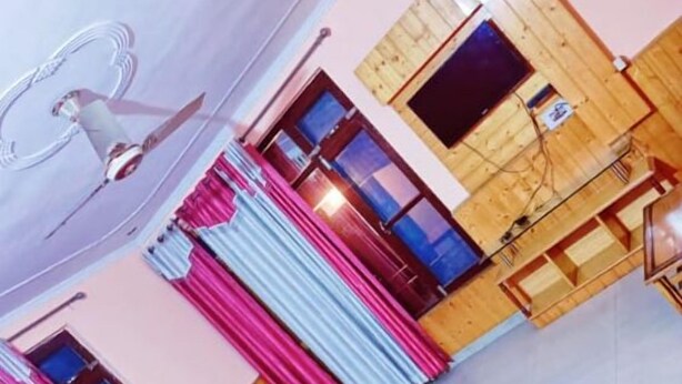 Una habitación con techo de madera, televisor y ventana con cortinas.