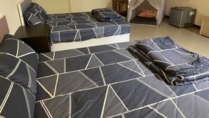Habitación con dos camas, cada una con cubrecama de estampado geométrico, una cama tipo dosel pequeña con luces, un refrigerador y una maleta.