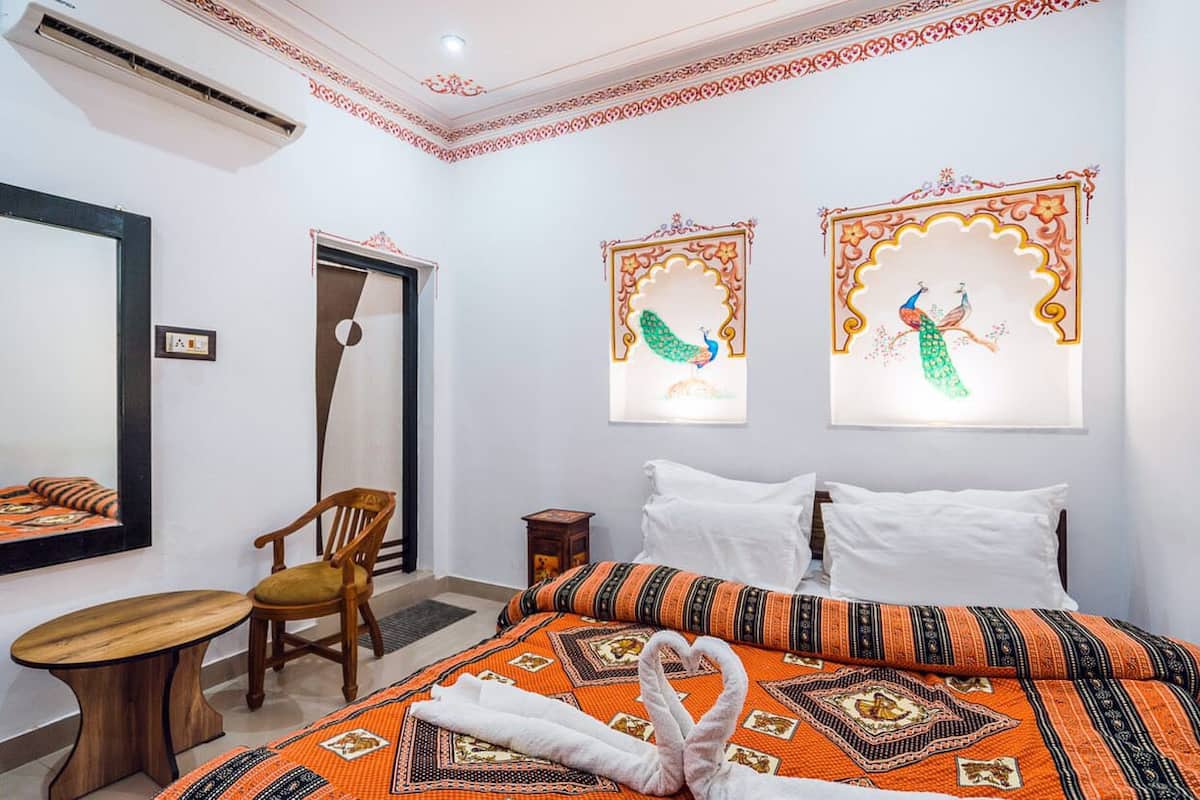 A hotel room with a bed, a chair, a small table, and two wall-mounted artworks.