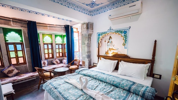 A traditional room with a bed, a bench with cushions, a small table, and a chair. - Lassi Guest House (Udaipur)