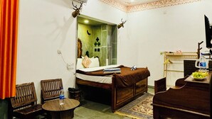 A hotel room with a bed, a wooden table, a chair, a small round table, and a ceiling fan. - Lassi Guest House (Udaipur)