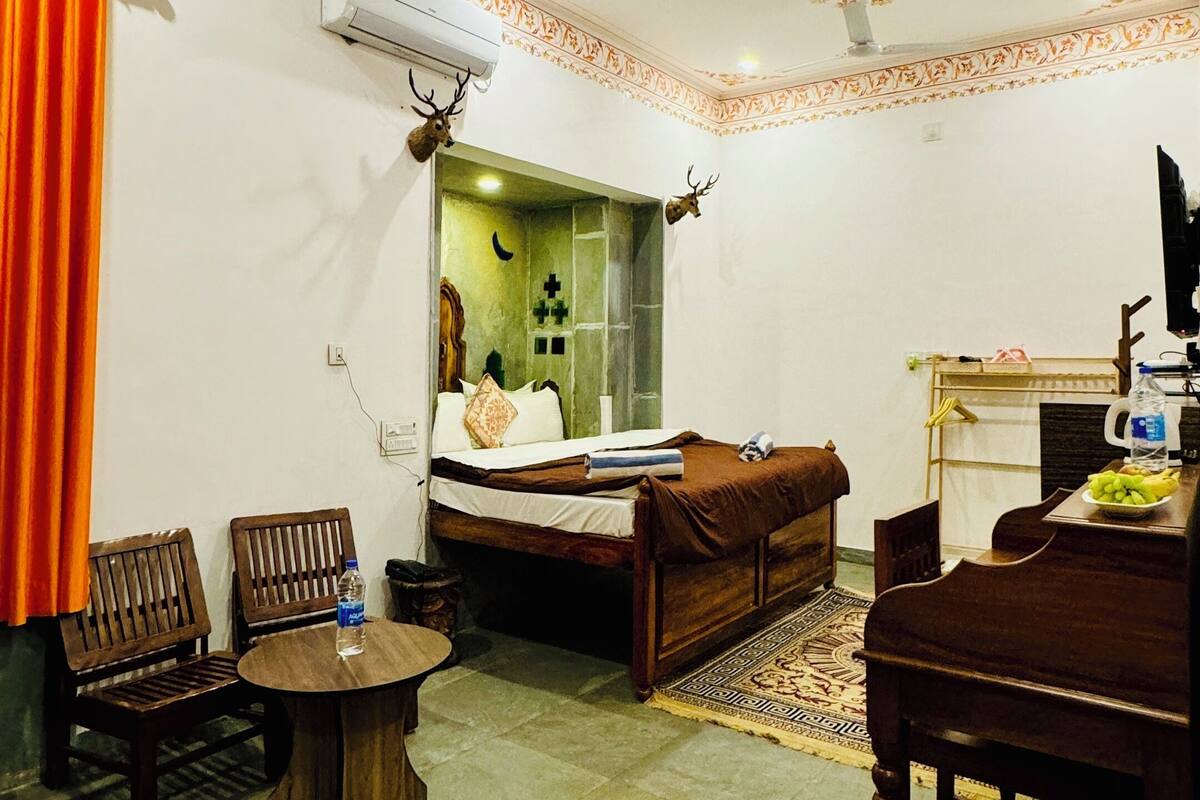 A hotel room with a bed, a wooden table, a chair, a small round table, and a ceiling fan.