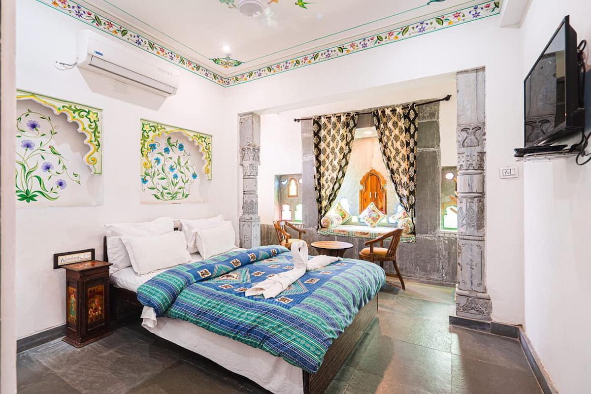 A hotel room with a bed, a small table with chairs, a TV, and decorative wall panels.