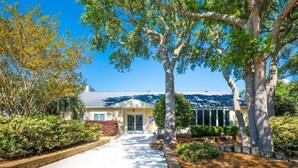 A residential house with a front yard, a driveway, and a large tree in the center.